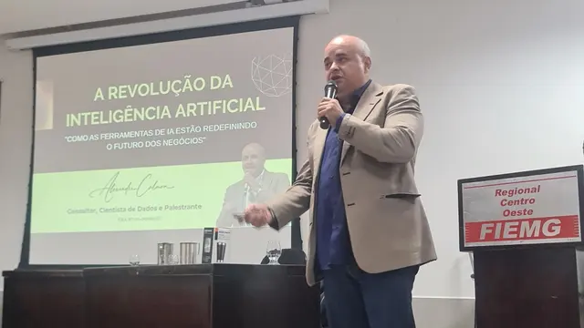 Alexandre Calmon ao microfone no palco da FIEMG, Regional Centro-Oeste, ao lado do telão