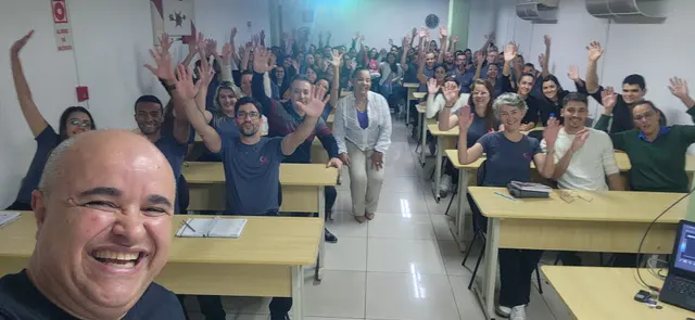 Alexandre Calmon sorrindo em primeiro plano, com a plateia de braços levantados ao fundo